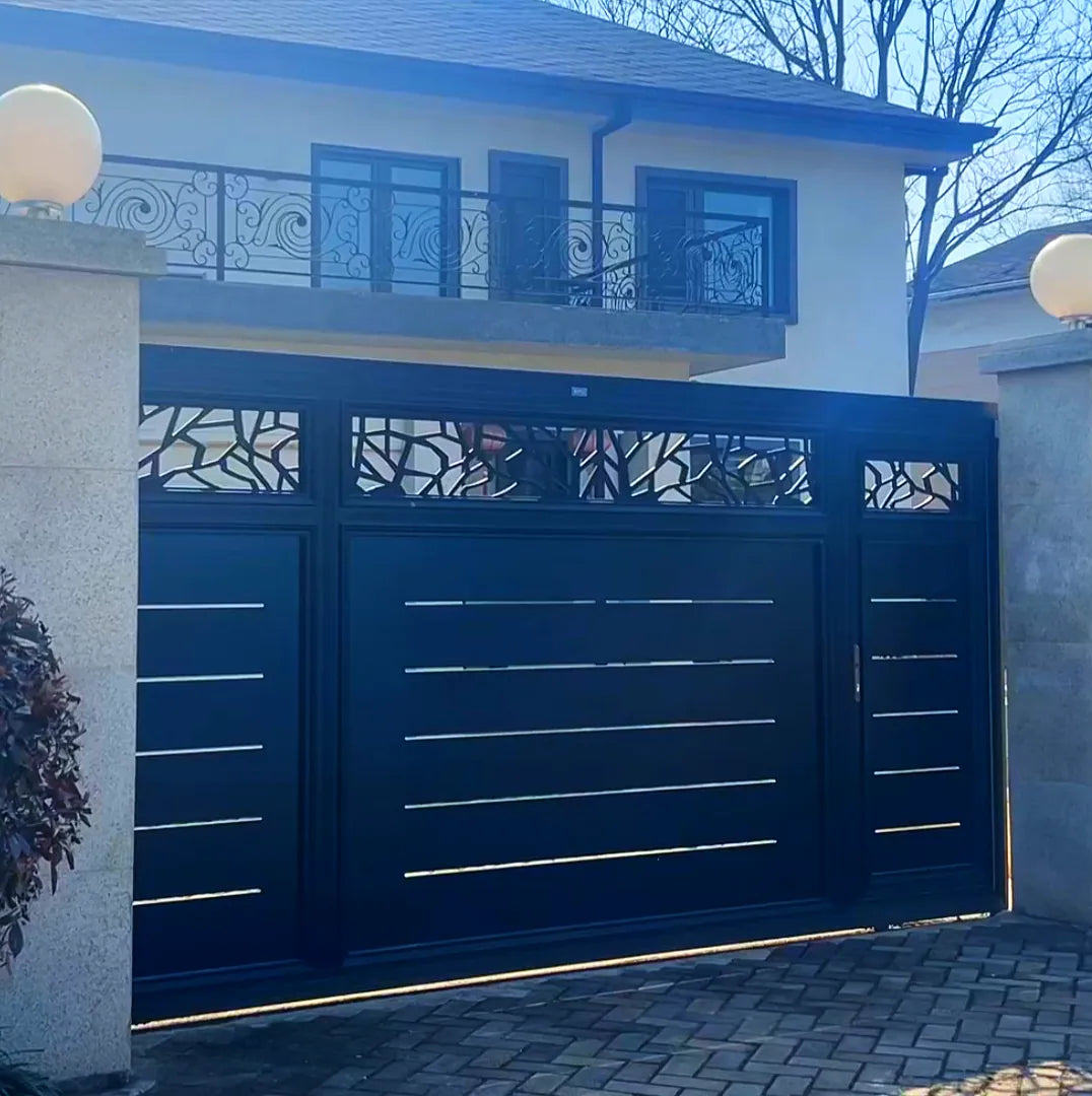 Installation photograph supplied by the works: Navy aluminium driveway gate with flat leaves, thin horizontal reveal slots and a laser-cut branch pattern across the top band, matching the balcony railing above.